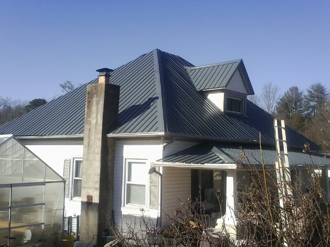 Dark blue standing seam metal roof on a white farmhouse with dormer — Slate & Tile Roof Repair by Roofing Brothers in Castleton