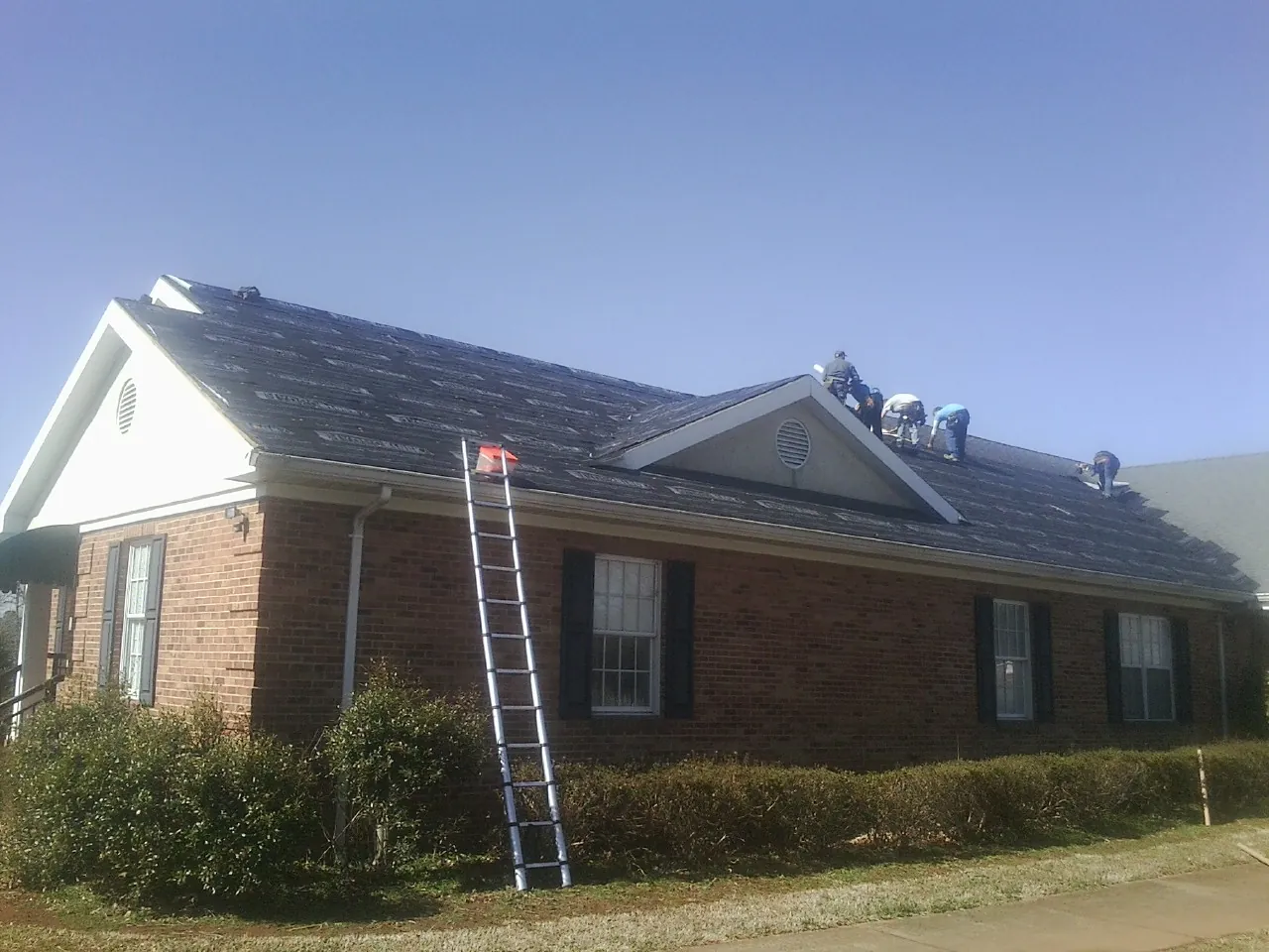 Crew tearing shingles off a brick ranch roof with a ladder set — Emergency Roof Repair work by our crew in Castleton