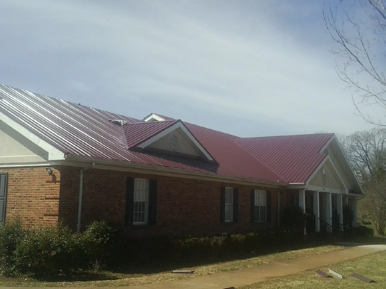 Red metal roof with gabled entries on a long brick building, from a Hail Damage Roof Repair job in Castleton