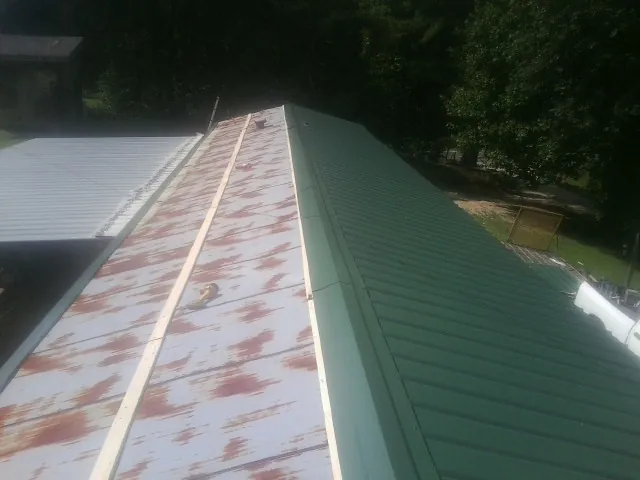 Old rusted panels beside newly installed green metal roofing — Wind Damage Roof Repair by Roofing Brothers in Castleton