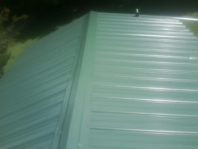 New green metal panels meeting at the ridge of a roof — Flat Roof Repair work by our crew in Castleton