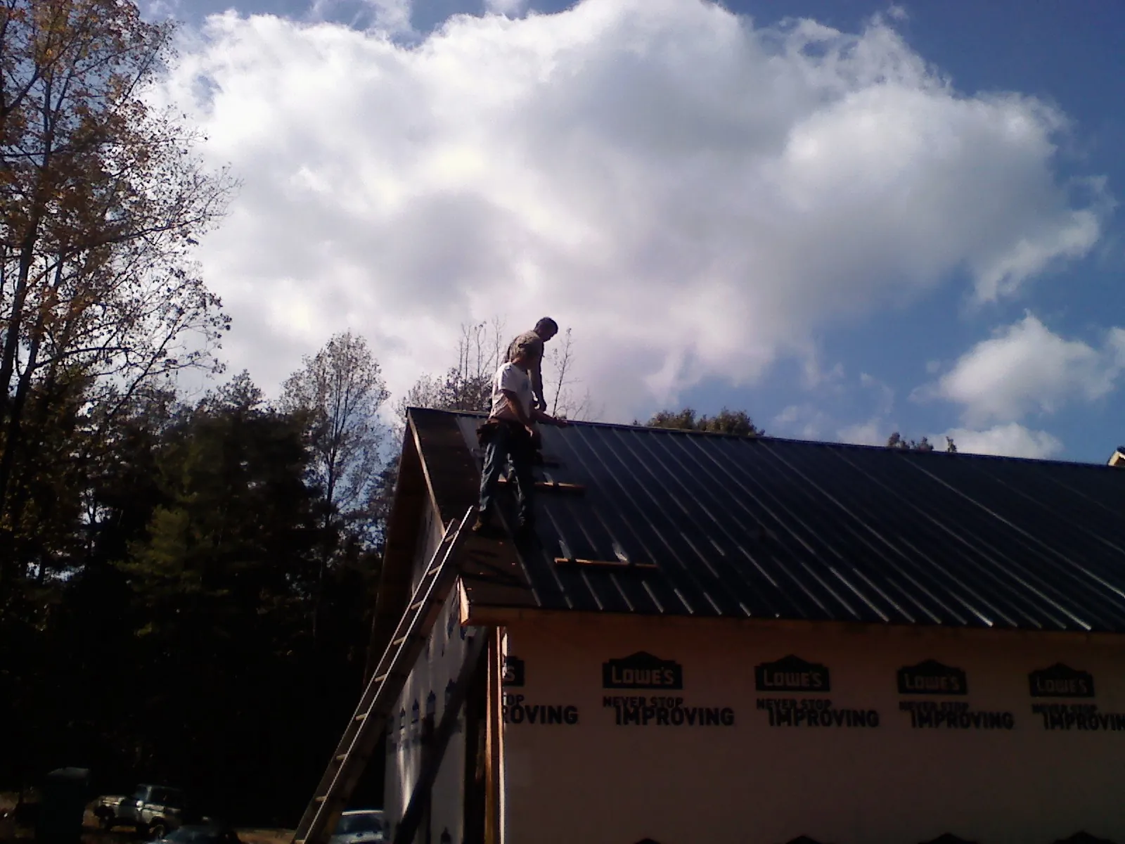 Roofer fastening dark metal panels high against a cloudy sky, from a Roof Inspection job in Castleton